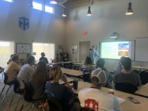 Lecturer and students in classroom previewing a presentation on a white board.