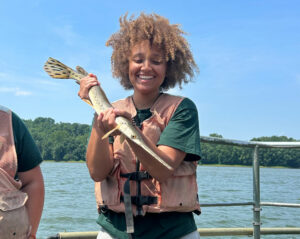 Intern student holding gar fish on a boat on the Ohio River.